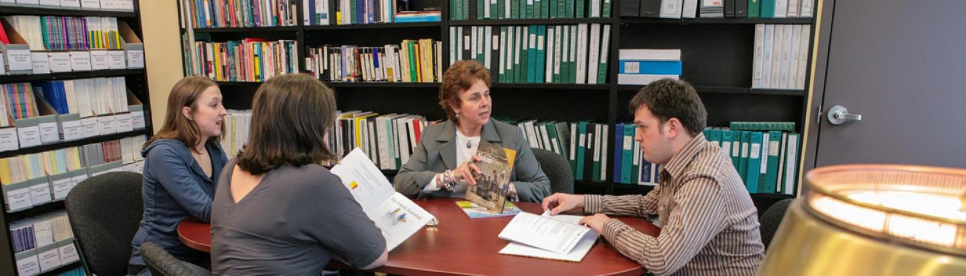 Dr. Deborah Berill sitting at a table with 3 students in an office surrounded by bookcases