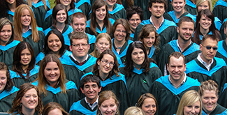 A large group of Teacher Education students wearing their convocation gowns smiling up at the camera for an aerial photo