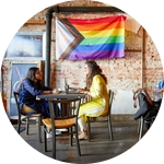 Students sitting in a coffee shop with a pride flag hanging above them