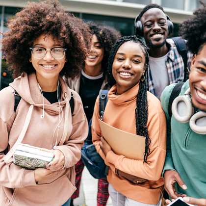 A group of Black identifying students smiling, wearing backpacks, and holding school items.