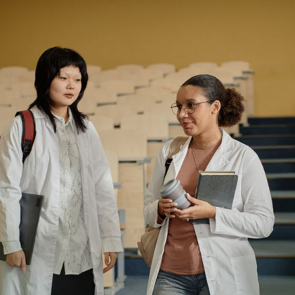 Two Trent University students wearing white lab coats stand in a classroom or laboratory setting.