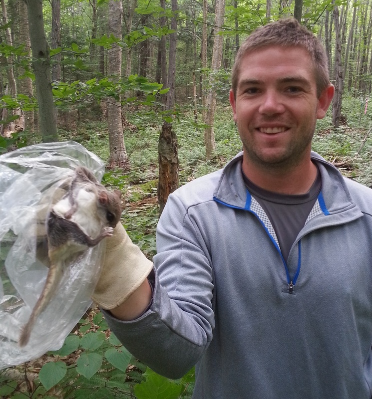 male student, michael brown, in a forest holding a field mouse with gloves smiling at camera