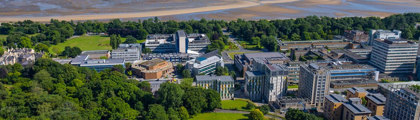 Aerial view of Swansea University, with buildings and a green wooded area right on the coast.