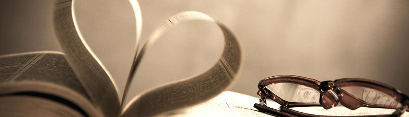 Book open with pages folded in a way thats making a heart shape, glasses placed near the far corner of the book