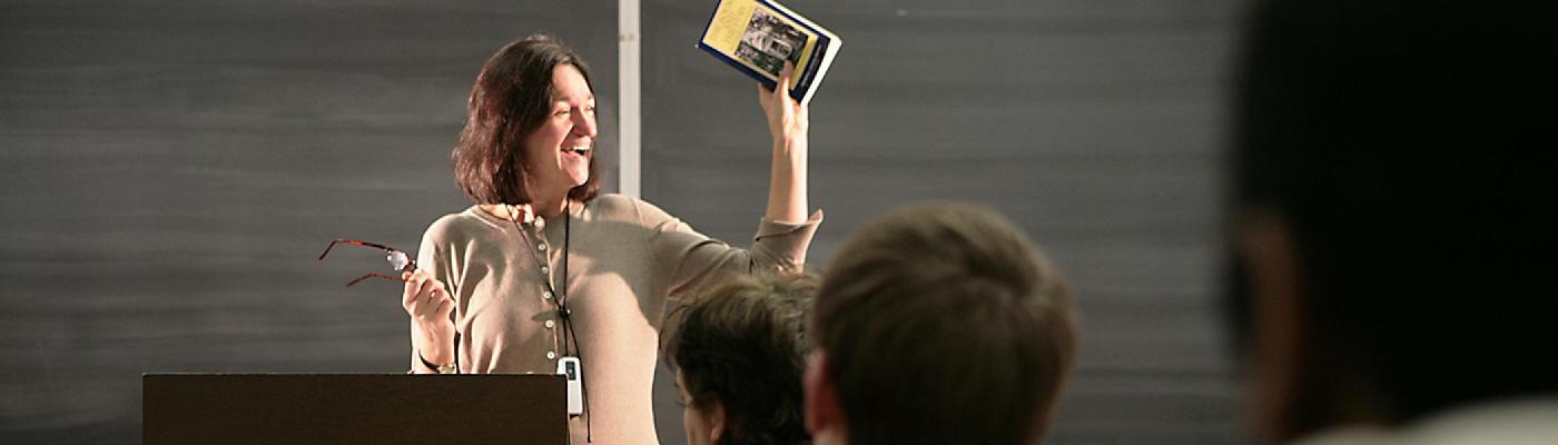 Faculty member in front of class holding up a book