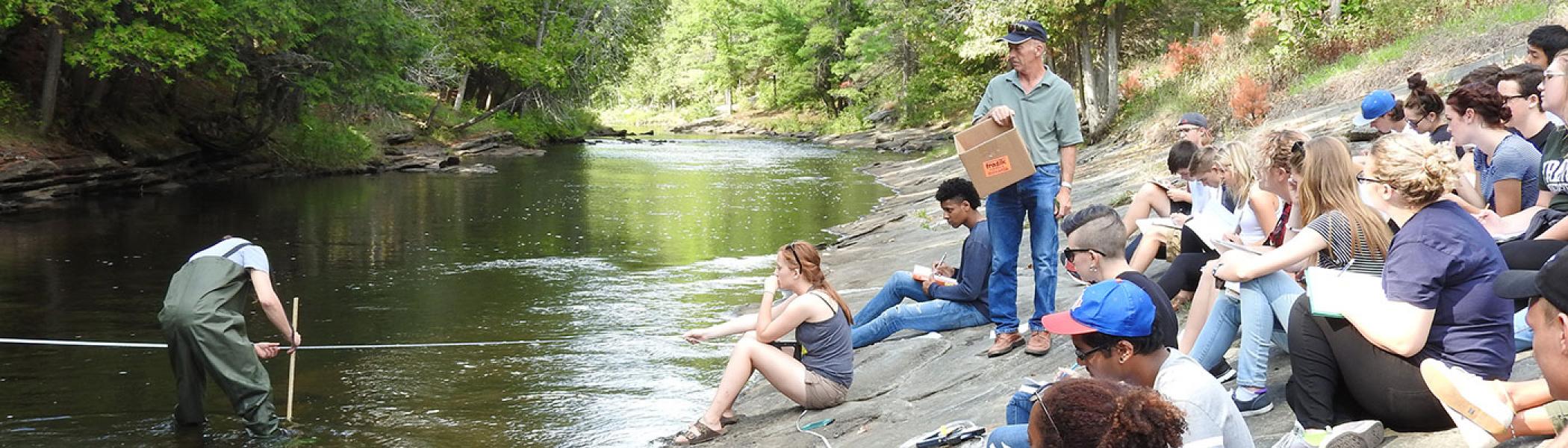 Student working on experiment in river while other students watch
