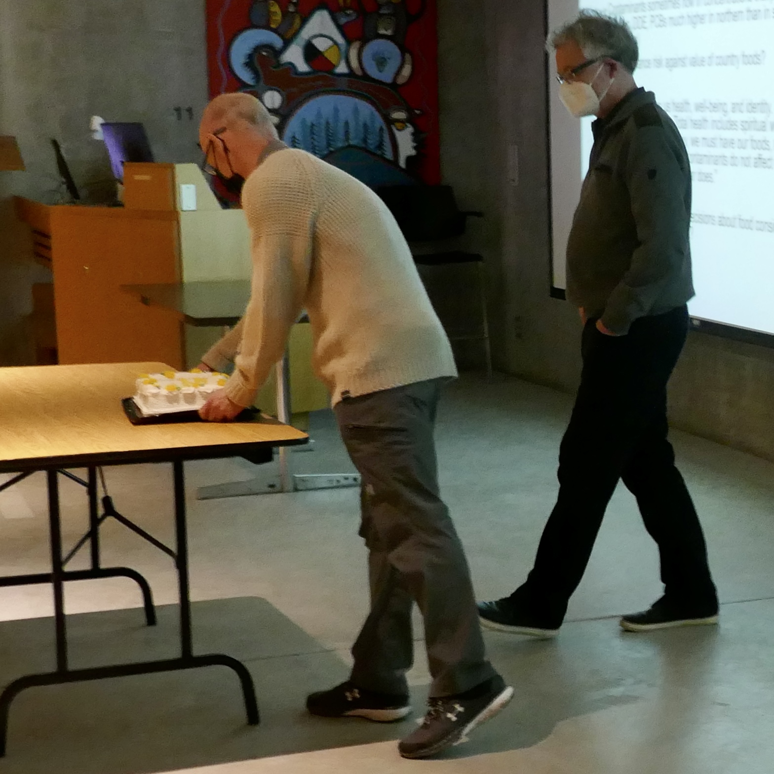 two white men in a classroom with a cake