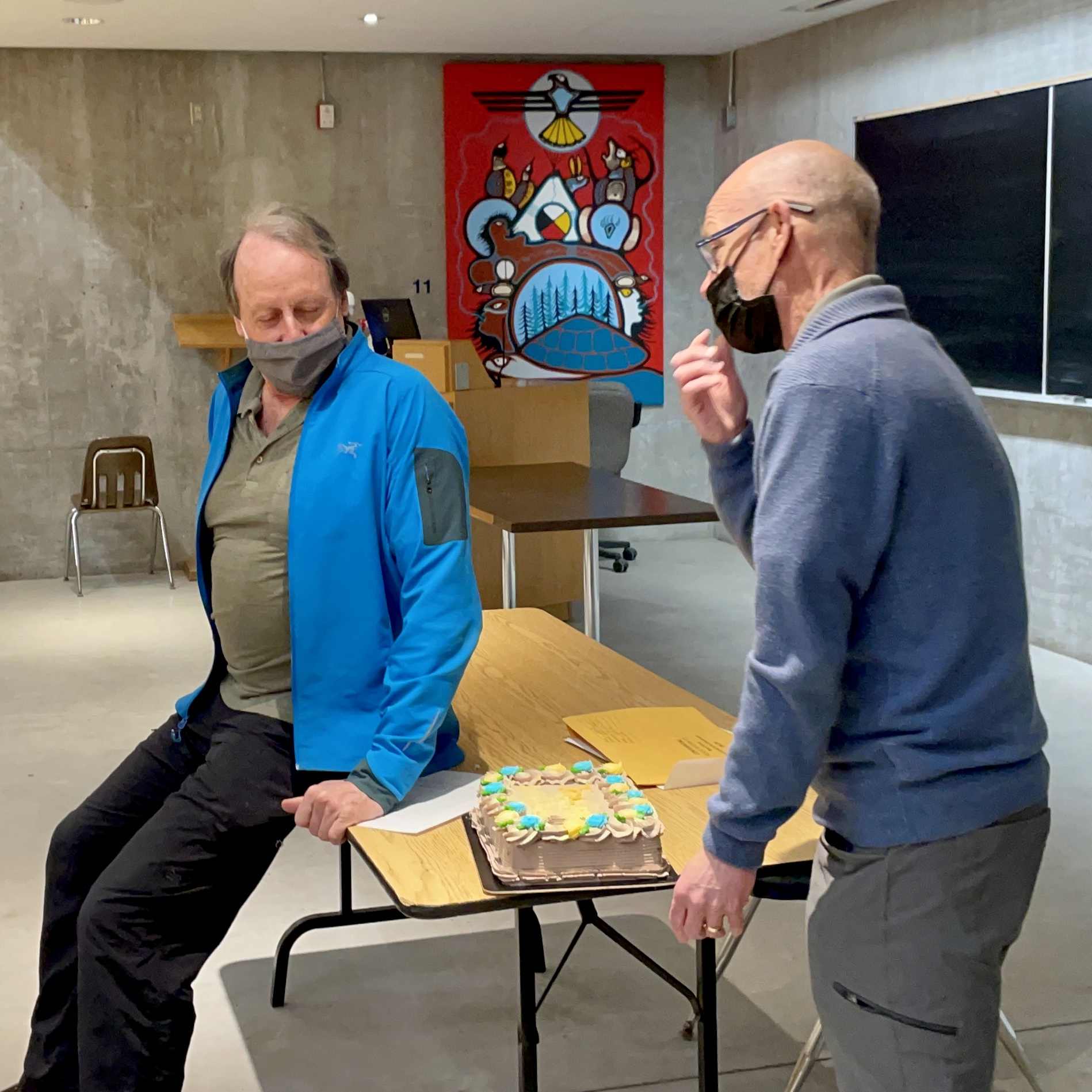 two white men in a classroom with a cake