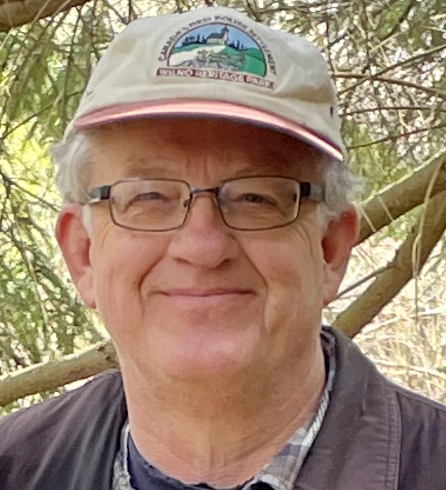 smiling man with pale skin wearing beige cap and trees in background