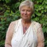person with pale skin and white hair wearing a white top against green leafy background
