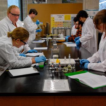 Students in white labcoats mixing samples in test tubes in a lab