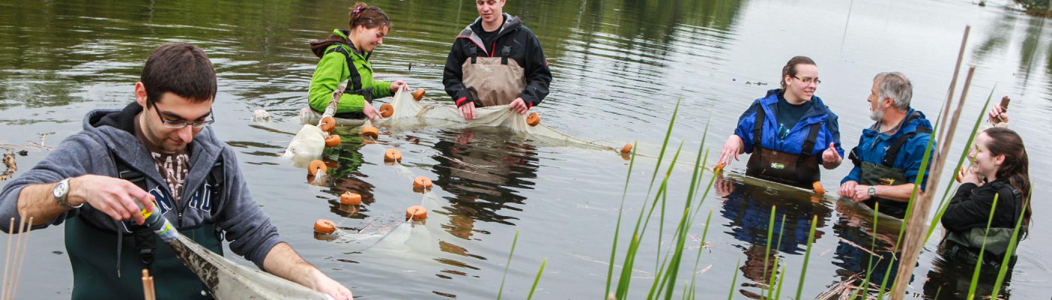 5 students standing in a river with a professor gathering water samples from nets