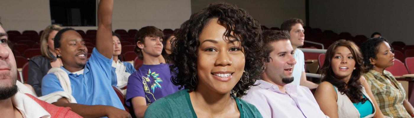 one woman sits in a classrooom with students around her