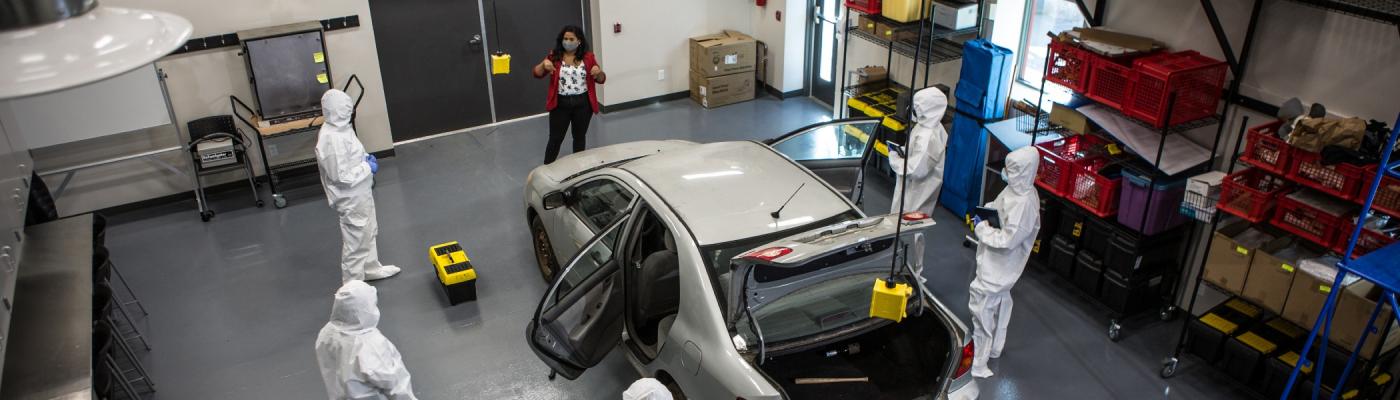 A group of forensics students working on a car while being guided by their instructor