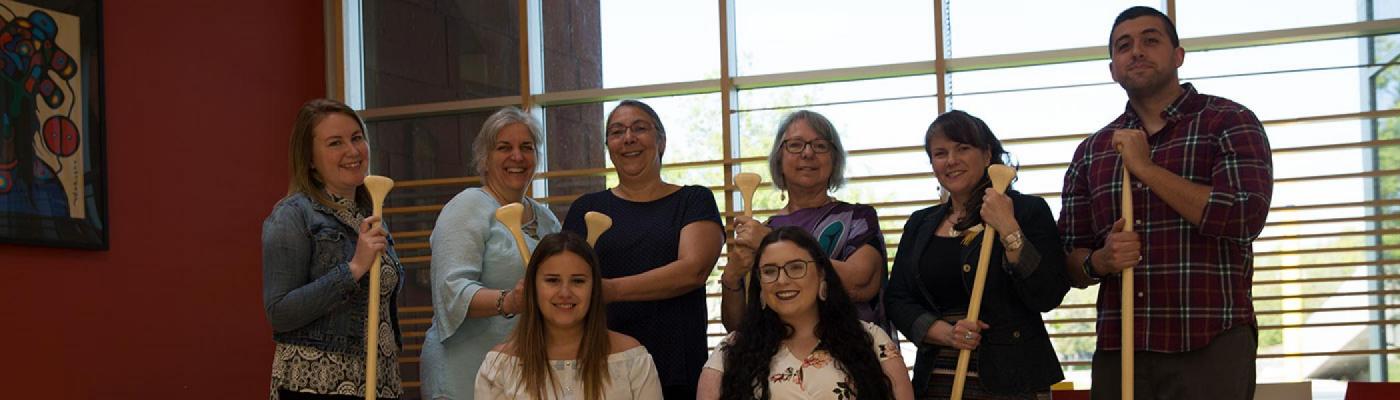 FPHL Department team holding paddles and posing for a group photo in the FPHL Gathering Space