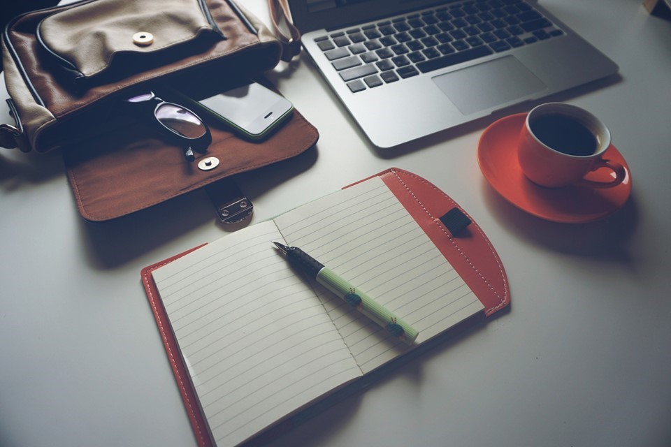 A desktop with a notebook, a pen, a laptop, and a cup of coffee