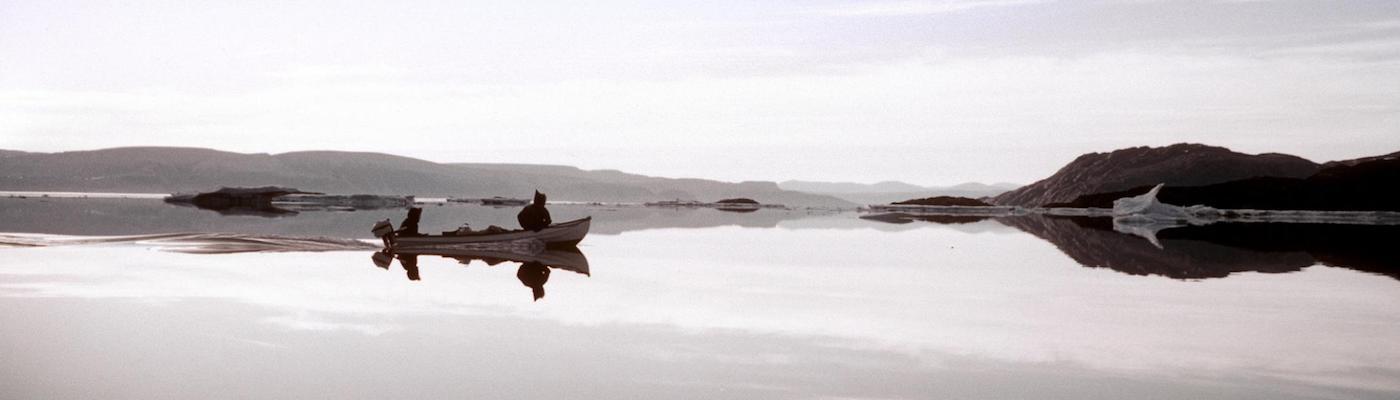 two men in a small motorized boat travel across arctic waters