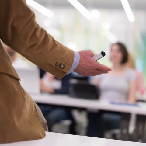 A close up of teacher hand with marker, while teaching lessons to students in classroom.