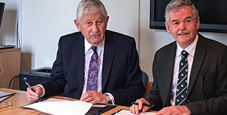 Dr. Leo Groarke sitting beside another gentlemen, signing papers at a desk