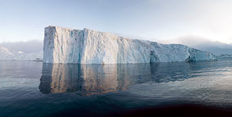 Iceberg floating in water against a pale blue sky