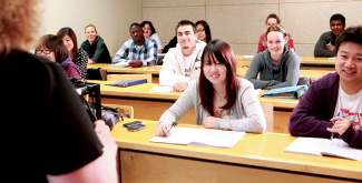 A group of students sitting at desks in rows looking at a professor