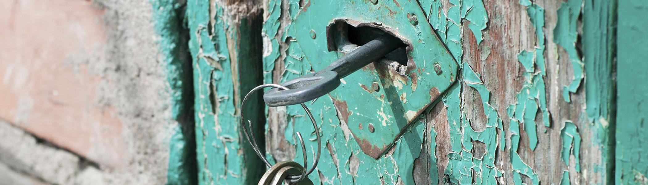 Old skeleton key in an old wooden door with chipped and peeling teal paint