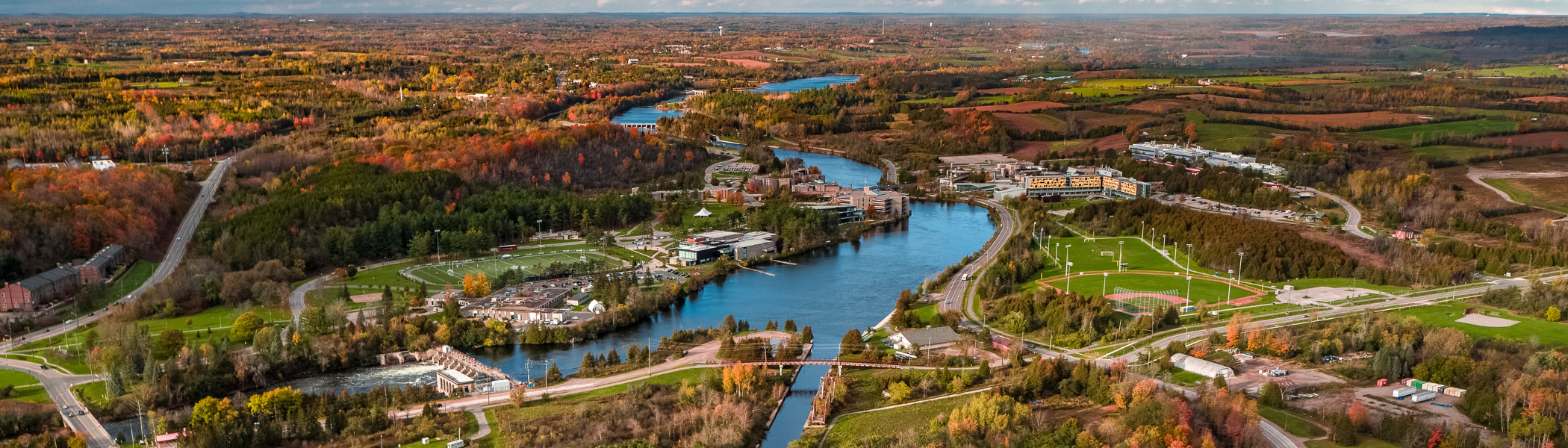 Aerial image of Symons campus, with the river and fall trees in the background.