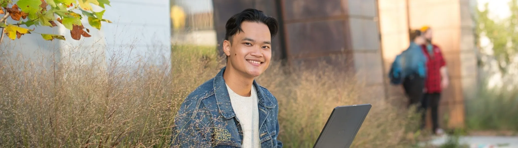 Student smiling at camera, on laptop.