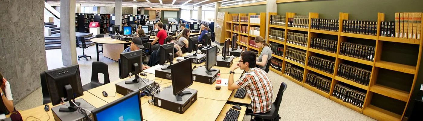 Students sitting at computers studying in the library surrounded by book shelves