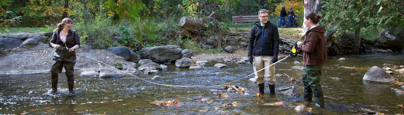 2 Students standing in the Otonabee river taking river samples in the spring time with Professor Paul Frost