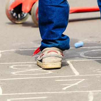 2 young children playing hopscotch on the concrete in a playground