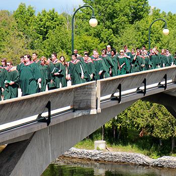 Student crowd of graduating students walking across the Faryon bridge during convocation on a sunny afternoon
