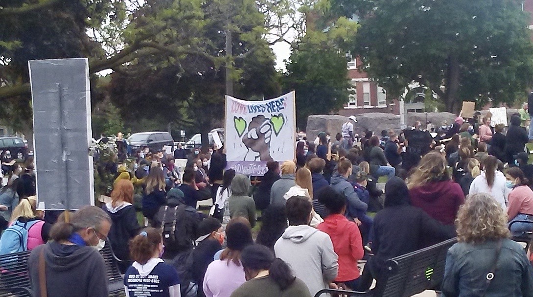 a banner held aloft in a crowded park that reads "love lives here"