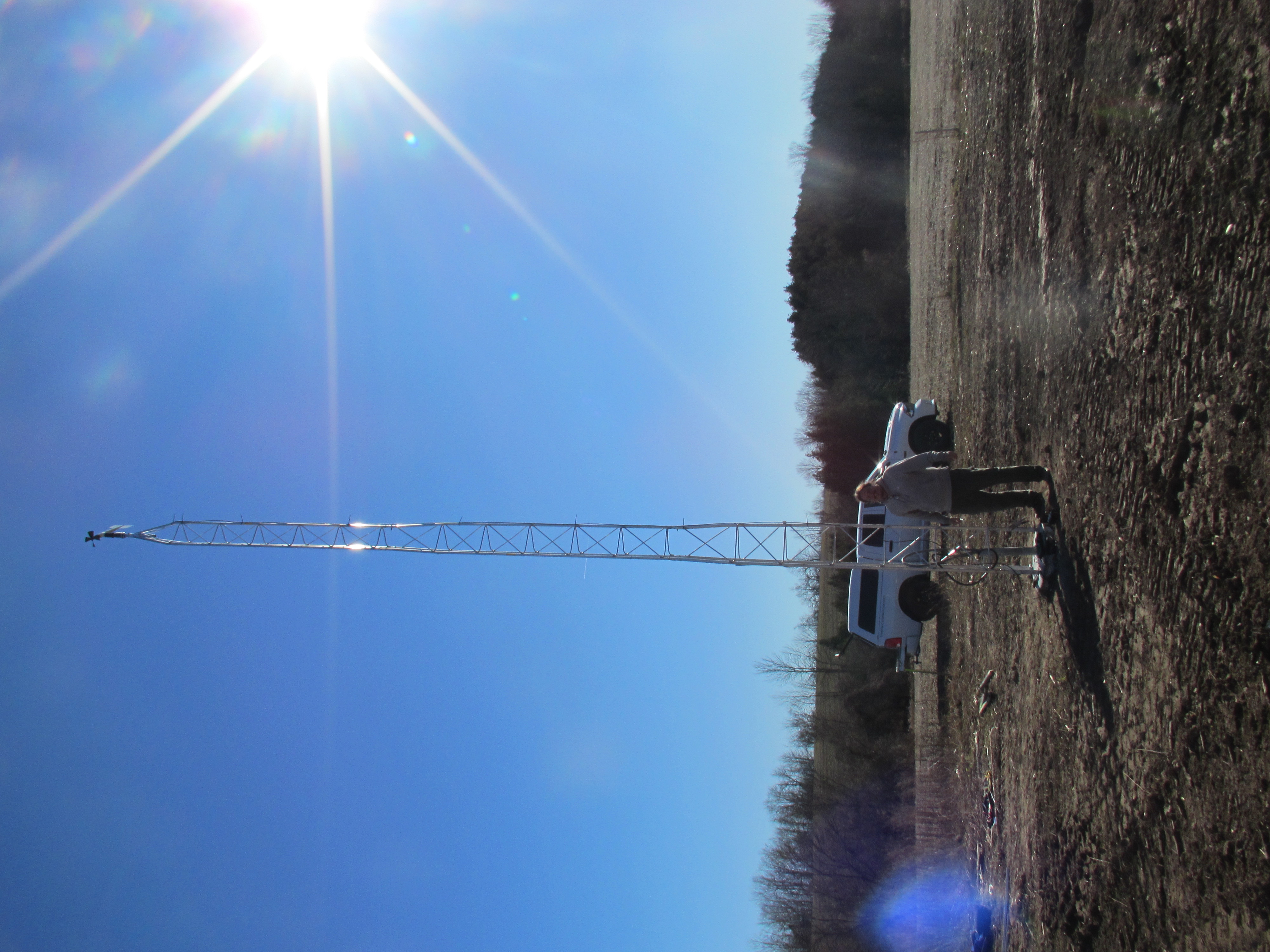 white tower against blue sky with sun shining rays; white man wearing beige jacket and brown pants; brown field; white truck