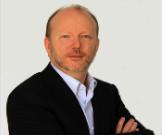 Andrew Stewart wearing a suit against a white background and smiling into the camera