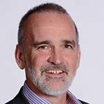 Scott Sinclair is against an off-white background and smiling at the camera 