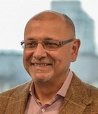Saäd Rafi wearing glasses and a brown jacket, smiling into the camera