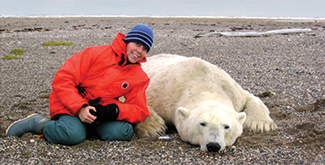 A student in a red raincoat sitting next to a tranquilized polar bear in the arctic tundra