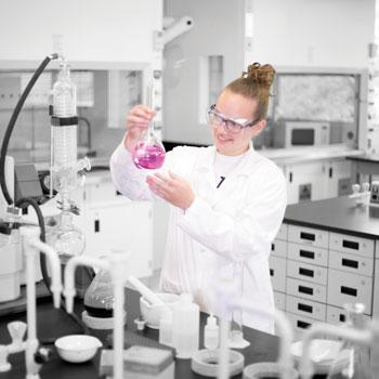 A girl wearing a lab coat a smiling in a lab