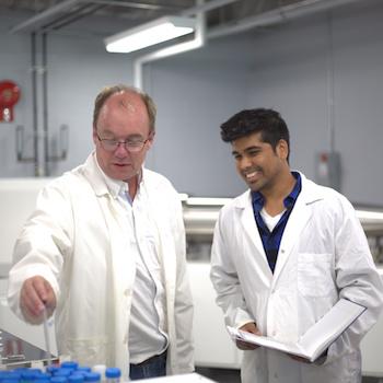 International Graduate student wearing lab coat working with professor. 