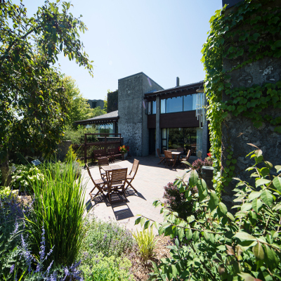 Back patio area of the Alumni house with patio furniture and plants surrounding the exterior of the building