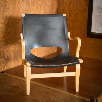 An original Ron Thom black leather chair with wood arm rests and a hole at the lower back of the chair