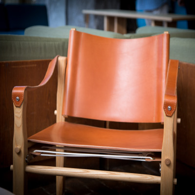 Orange leather chair with straps as arm rests and string supporting the seat 