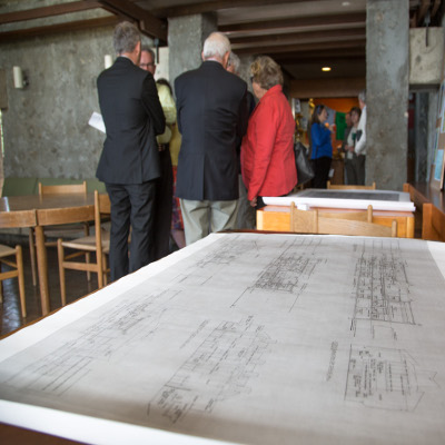 A photo of a group of people surrounding a original plan of an non-labeled building of Trent