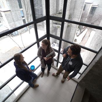 Three students standing in front of a big window with Champlain College in the backgrond