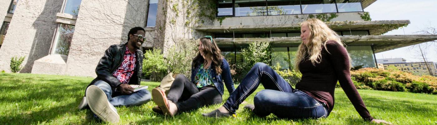 3 History students sitting on the grass in front of the Bata Library chatting