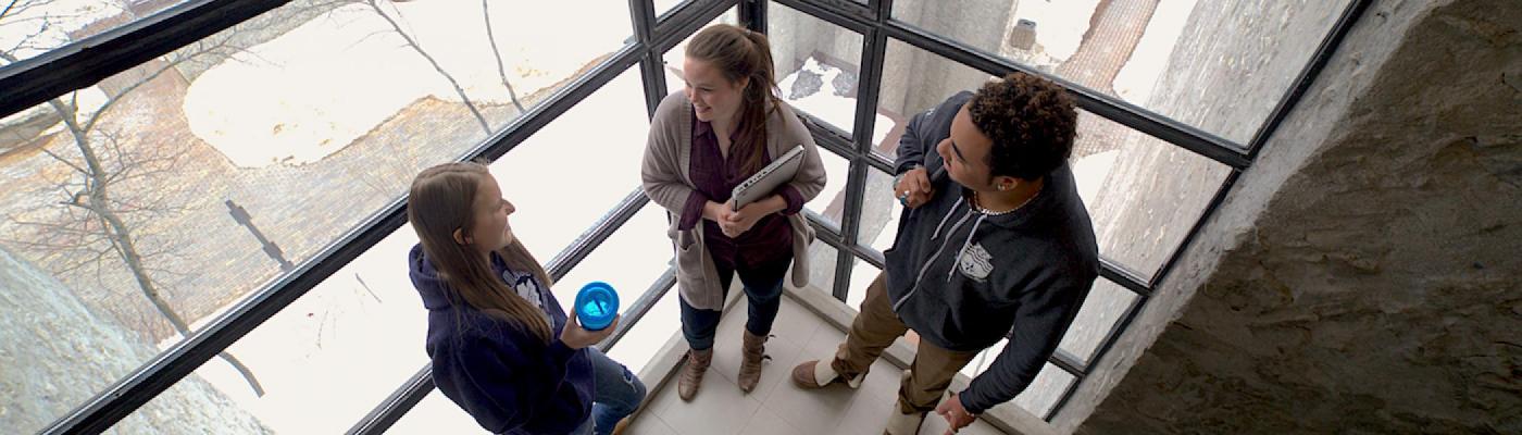 Three students standing in front of a big window with Champlain College in the backgrond