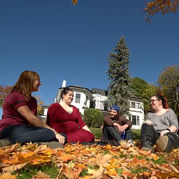 4 people sitting on the grass outside of Traill College