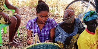 A student collecting grass in a wicker basket in Ghana with other local women