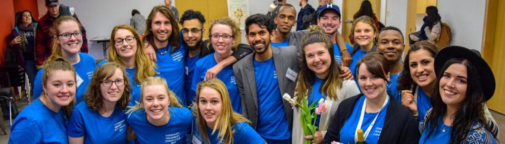 A group of students huddles together in a classroom, wearing blue t-shirts, smiling at the camera